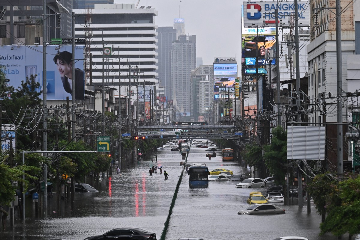 People wade along flooded Petchaburi Road in Bangkok, with vehicles partly submerged, on 26 September 2026.
